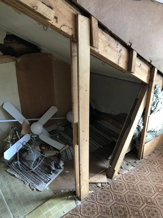 Rivningsarbete på vind med synlig stötta i mitten, bråte och en takfläkt på golvet.