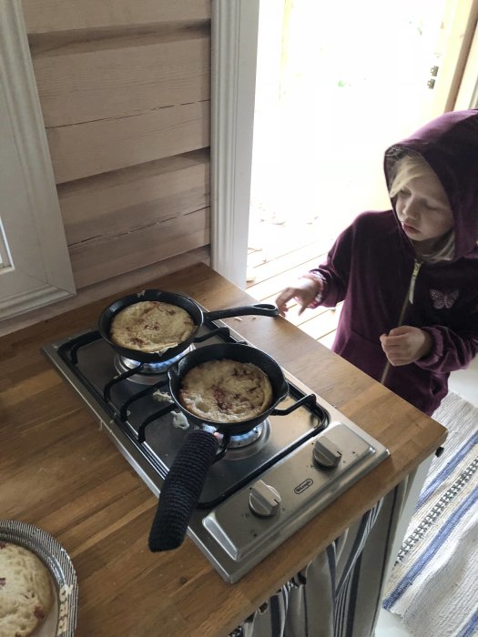 Barn i luvtröja lagar pannkakor på spis i ett hemmakök.