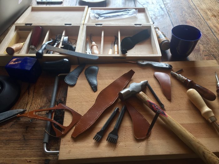Verktyg och läderdelar för hantverk av växelspaksknopp spridda på ett träbord.