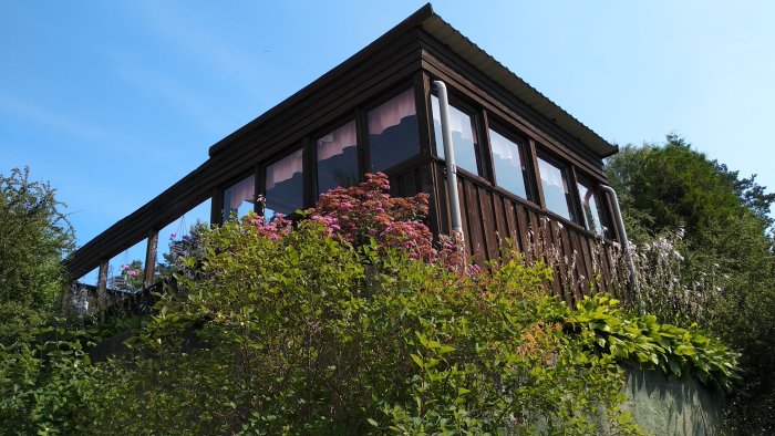 En villa belägen i en slänt med utjämnad mark framför och en gammal mur i tre steg, omgiven av grönska och blommor.