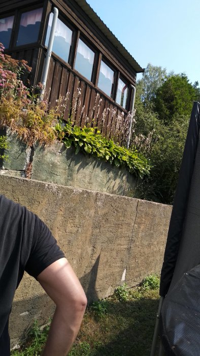 Gammal oarmerad stödmur i tre steg framför villa i sutteräng med vegetation.