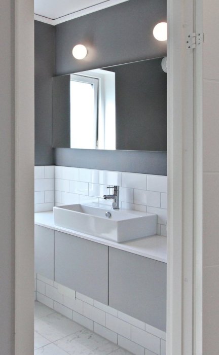 Renoverat badrum med vita kakelväggar, rektangulär handfat på MDF-skåp och spegel ovanför.