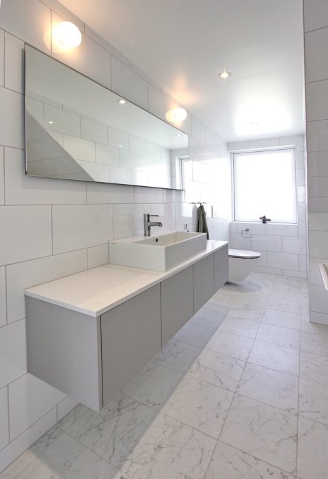 Modern renoverad badrum med vit kakel, stor spegel och inbyggd MDF-förvaring.