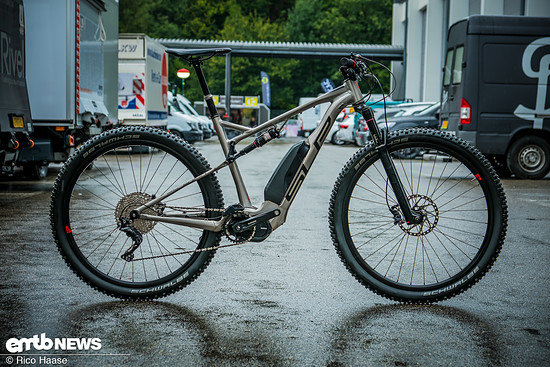 Ny mountainbike parkerad på asfalt med full dämpning och el-assistans, redo för stigcykling.