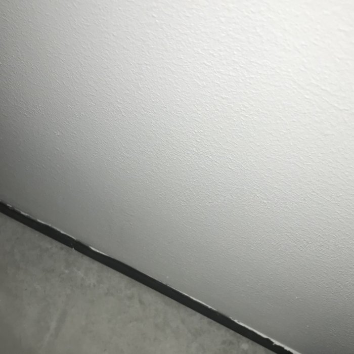 Vägg möter betonggolv med svart list som går upp några cm på väggen.