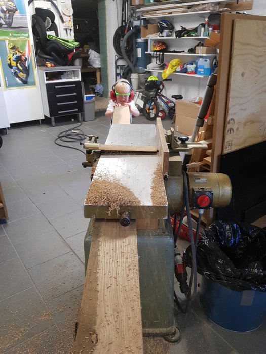 Barn använder en hyvelbänk för att hyvla ett trästycke i en verkstad.