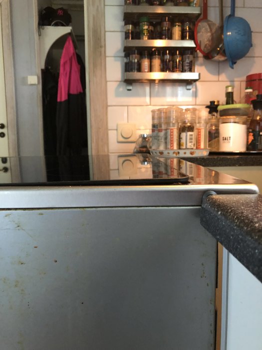 Köksdisk med baktill speglande yta som visar kryddhylla och rosa handduk, ger intryck av ordning och renlighet.