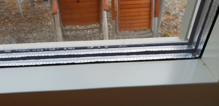 Närbild på ett fönsters tätning med synliga skador och tecken på läckage mellan glasrutorna.