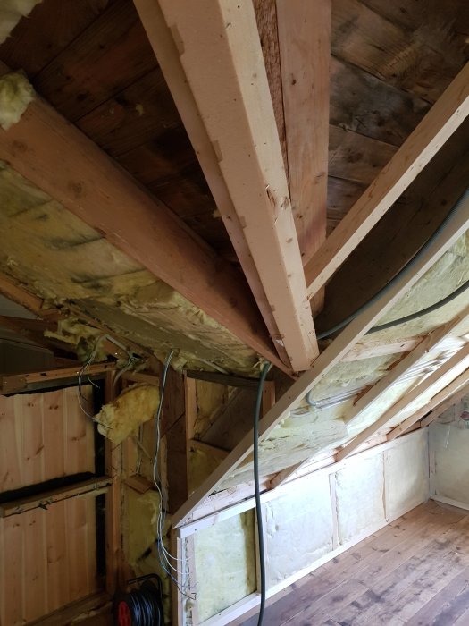 Ett vindrum under renovering med exponerade takstolar och delvis borttagen isolering i väggfack och tak.