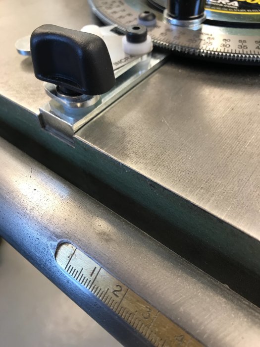 INCRA anhåll på en sågbordsskena bredvid ett måttband som illustrerar skillnaden i spårdjup.