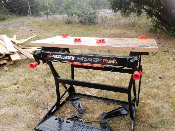 Black & Decker Workmate arbetsbänk med trasig vit rem, placerad utomhus med brädor i bakgrunden.