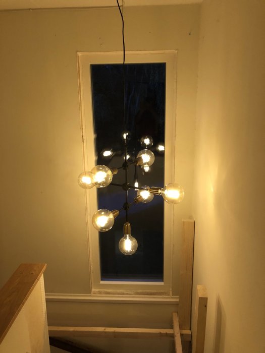 Nyinstallerat vertikalt fönster med tänd modern taklampa framför i en trappa under renovering.