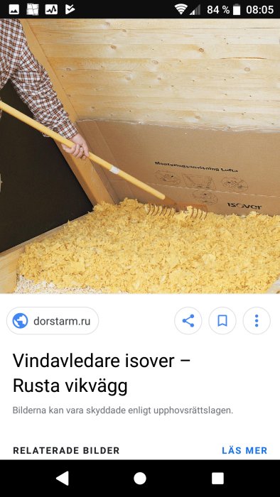 Person som isolerar en vind med lösull och håller i en räfsa vid en trävägg.