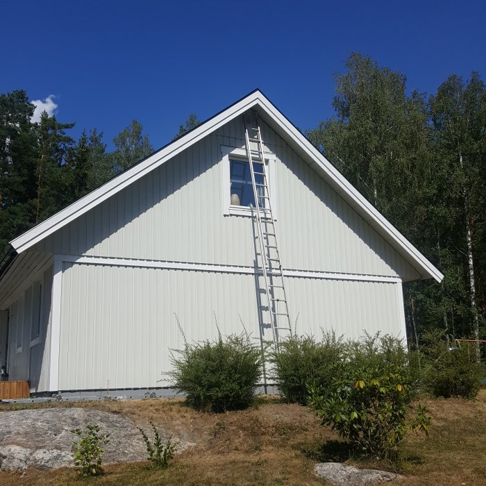 En stege lutad mot husgaveln på ett nymålat vitt hus med blå himmel i bakgrunden.