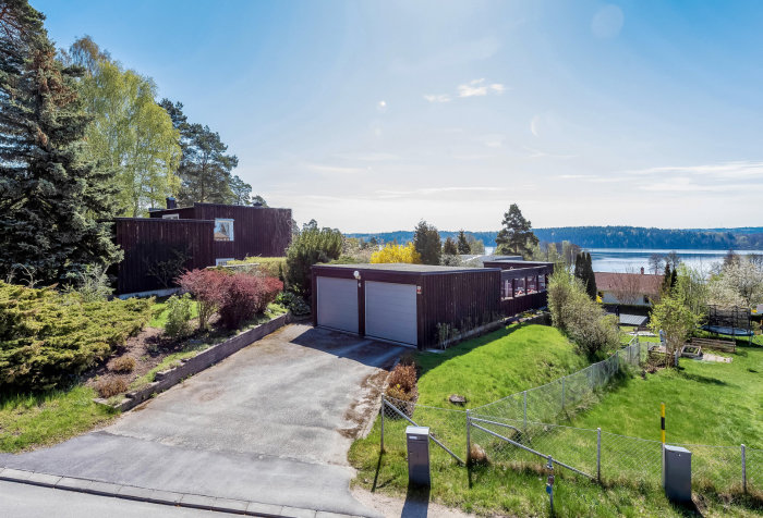 Vy över ett fristående mörkt dubbelgarage bredvid en villa, med en vidsträckt utsikt över en sjö i bakgrunden.