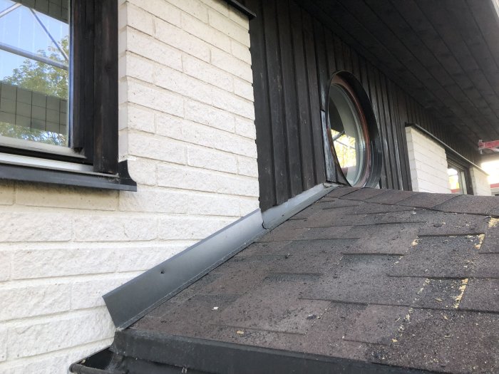 Exteriör vy av husfasad med stående panel och runda fönster utan foder.