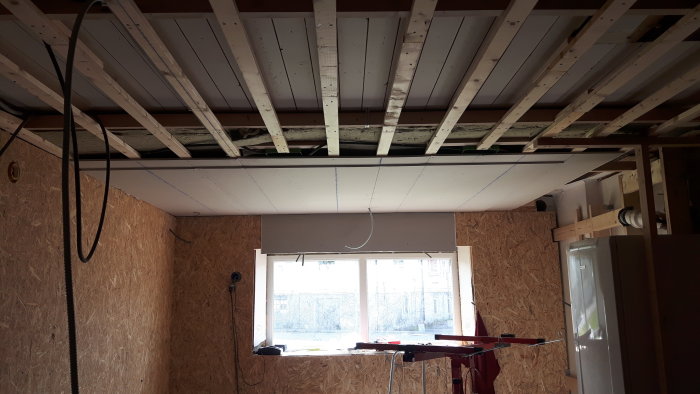 Nyinstallerade gipsskivor på ett tak och en vägg i ett pågående byggprojekt med synliga träreglar.
