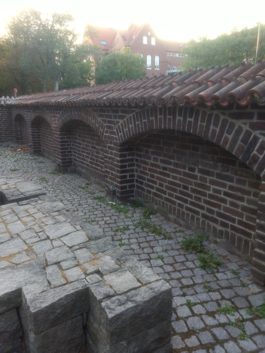 Röd tegelbåge som liknar Roskilde-mur mot bakgrund av stadsmiljö och stenlagd mark.
