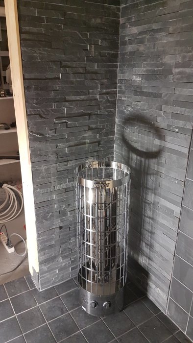 Rostfri elektrisk bastuugn av märket Harvia i ett hörn med mörka skifferstenar.