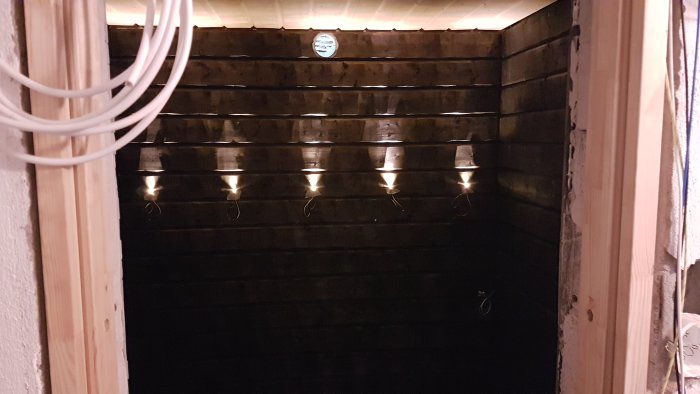 Mörkt träutrymme med rader av inbyggda taklampor som avger mjukt ljus, med synlig kabelnät i framkant.