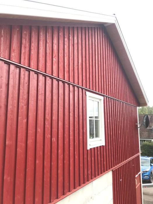 Röd träfasad med råspont synligt under takkanten ovanför ett fönster.