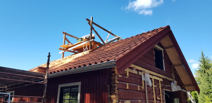 Person blandar bruk på tak till ny murad skorsten på rött taktegelhus under klar himmel.