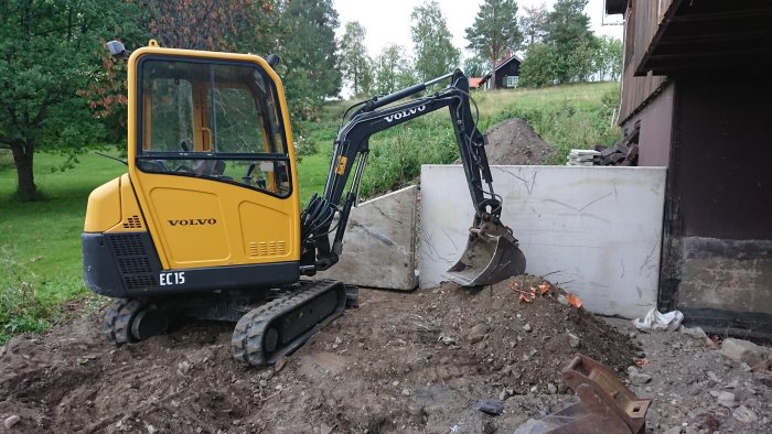 Minigrävare vid L-stödsmurar på byggarbetsplats förbered för carportkonstruktion.