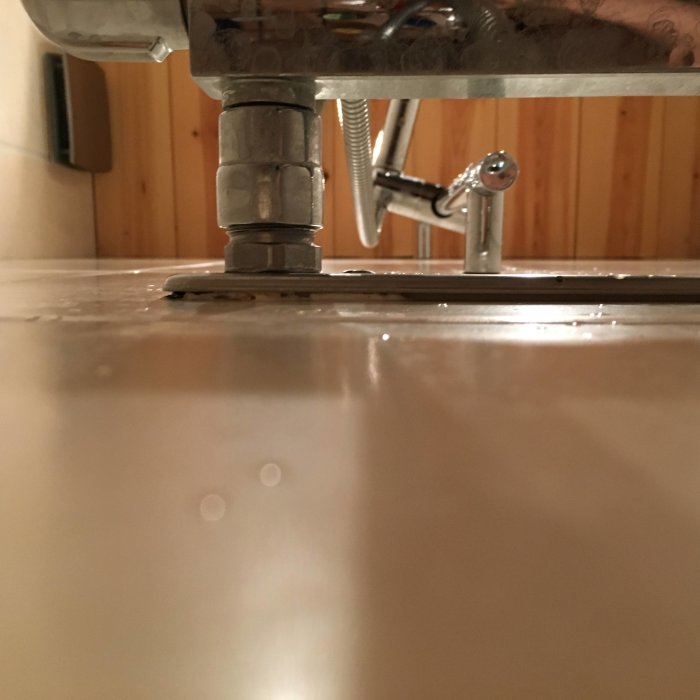 Glipa och silikonrester synliga mellan en blandare och kakelvägg i badrummet, sett underifrån.