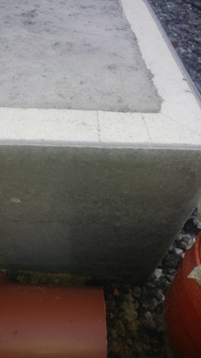 En betongsyll med skador på kanten vilande på polystyrenisolering och grus.