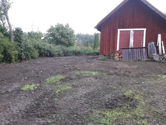 Bortschaktad jord runt röd vedbod, blivande grusyta framför.