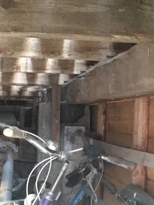 Undersida av en altankonstruktion med robusta plintar och tjocka träreglar samt en cykel i förgrunden.