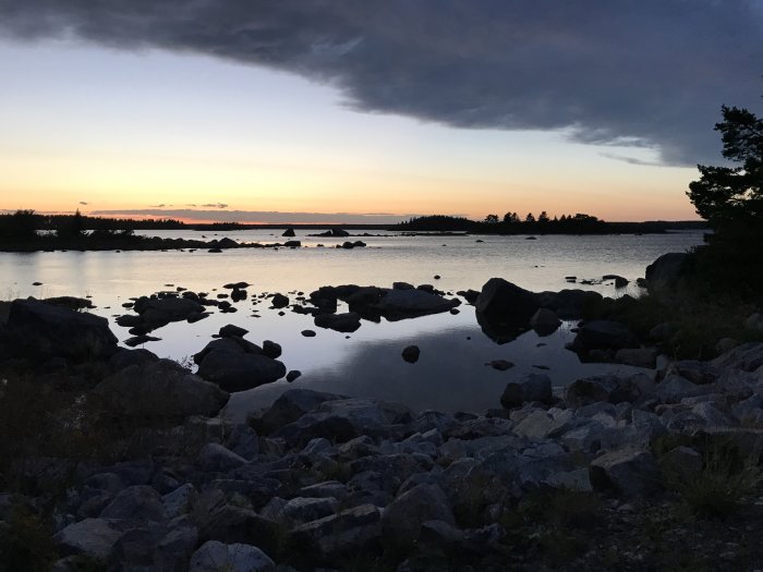 Solnedgång vid havet med steniga stränder och stilla vatten under skymningen.
