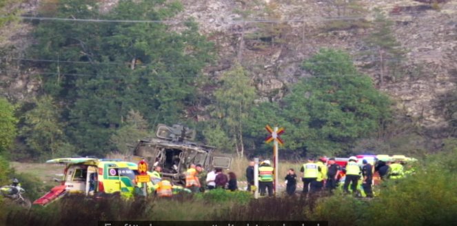 Räddningspersonal och fordon vid en olycksplats med en övervält bil nära järnvägskorsning.