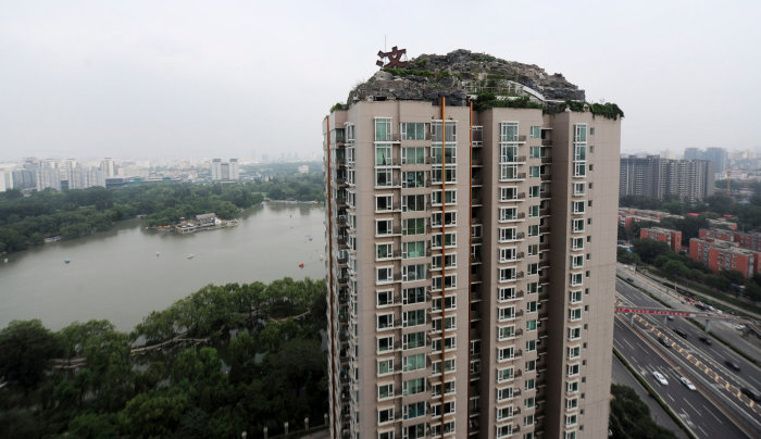 Hög byggnad med ett konstgjort berg på taket i Bejing, mot bakgrund av stad och vatten.