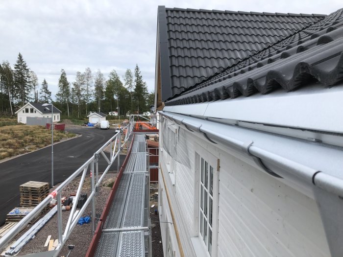 Utsikt från en byggställning visar nyklädd takfot och färdiga fönstersmygar på ett hus.