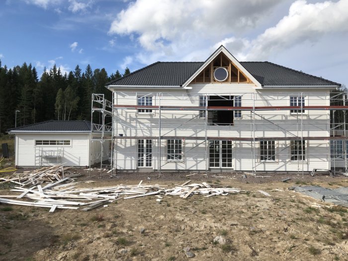 Hus under renovering med ställningar runt fasaden och oordnat träavfall på marken.