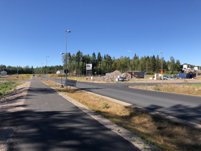 Vy över byggområde med nya hus och anläggningsarbete längs tre gator under en solig dag.