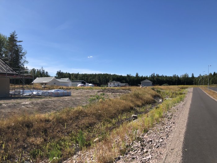 Byggområde med nyuppförda hus längs tre gator, byggmaterial och delvis obebyggda tomter i ett soligt landskap.