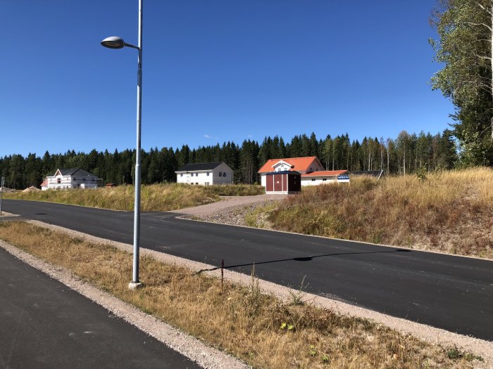 Byggområde med nyasfalterad gata och flera nybyggda hus omgivna av träd och en klarblå himmel.