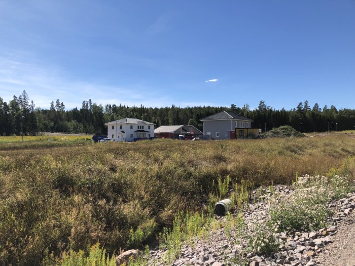 Nybyggda hus i ett utvecklande bostadsområde med öppna fält och skog i bakgrunden.