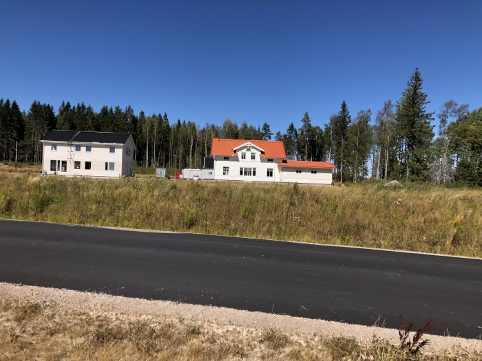 Byggområde med nyuppförda hus längs tre gator, växande gräs och skog i bakgrunden.