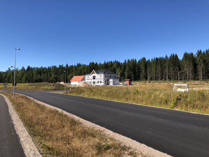 Uppfört hus bredvid en tom byggplats och tre gator i ett nytt bostadsområde med skog i bakgrunden.