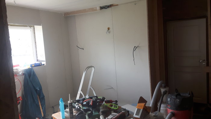 Renoveringsarbete i kök med nylagt gips på vägg och i tak, eluttag utanpåväggsmontage och byggmaterial i förgrunden.