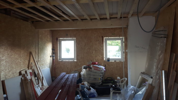 Renoveringsarbete i kök med exponerade reglar i taket, OSB-skivor på väggarna och byggmaterial utspritt.