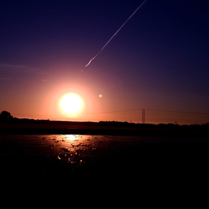 Soluppgång över ett öppet fält med vattenpölar som reflekterar solens ljus.
