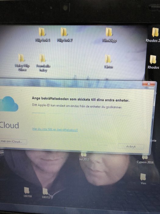 Skärmdump visar iCloud-verifieringsfönster på en dator med ikoner och suddig bild av två personer i bakgrunden.