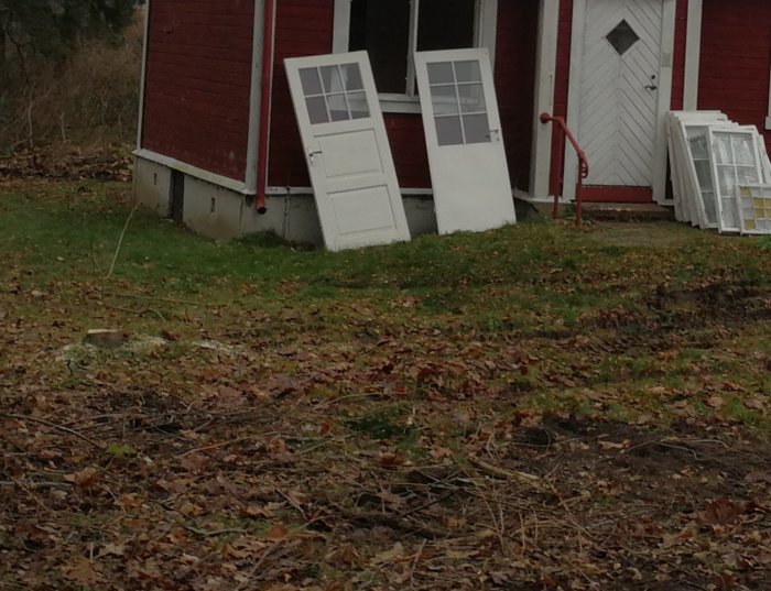 Telefonkabel synlig nere till vänster på husgrunden omgiven av löv och gräsmatta, med en röd stuga i bakgrunden.