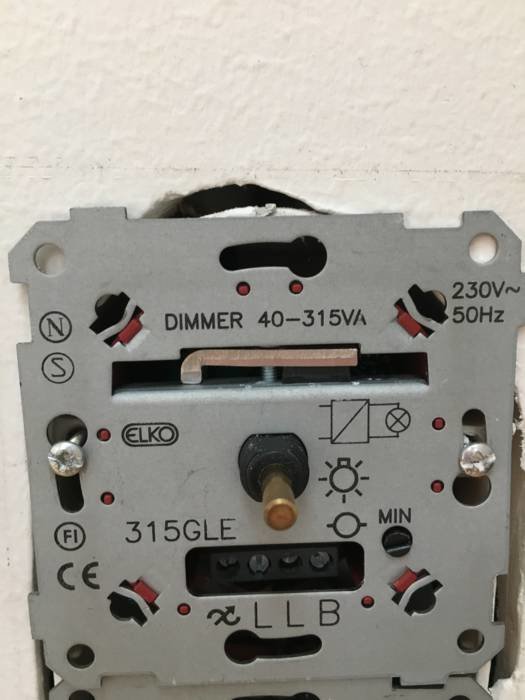 En grå eljo-dimmer med reglage och texten "DIMMER 40-315VA" monterad i en vägg utan täckplatta.