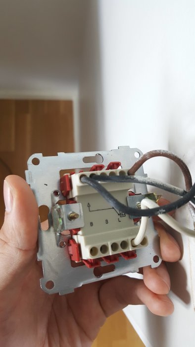 Hand håller en öppen elektrisk väggströmbrytare med synliga trådar och anslutningsterminaler.