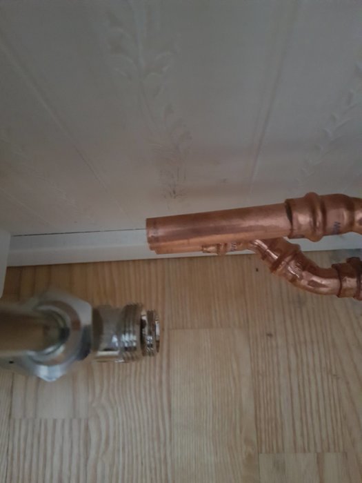 Kapade kopparrör nära vägg och golv med synligt radiatoranslutning.
